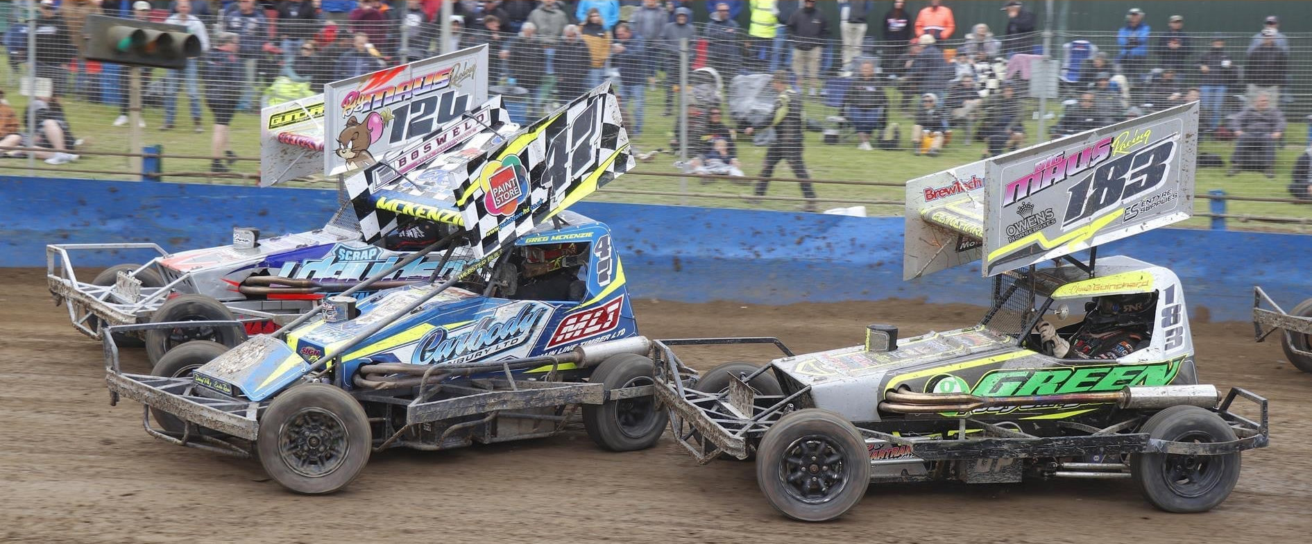 Two race cars on a dirt track with various sponsor logos displayed above.